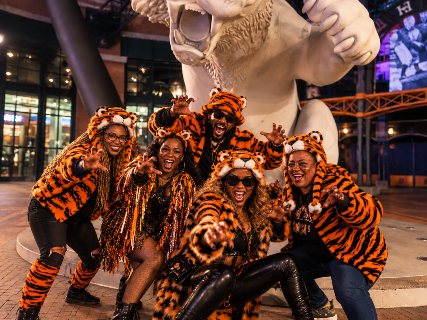 A stylish adult team in coordinated tiger-inspired costumes striking playful poses beside the Comerica Park tiger statues in Detroit